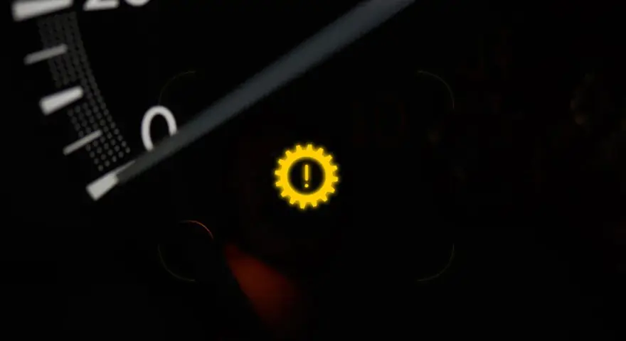 Gelbes Warnlicht mit einem Zahnrad und Ausrufezeichen im Auto-Armaturenbrett. Ein Zeichen für ein Problem mit dem Getriebe.