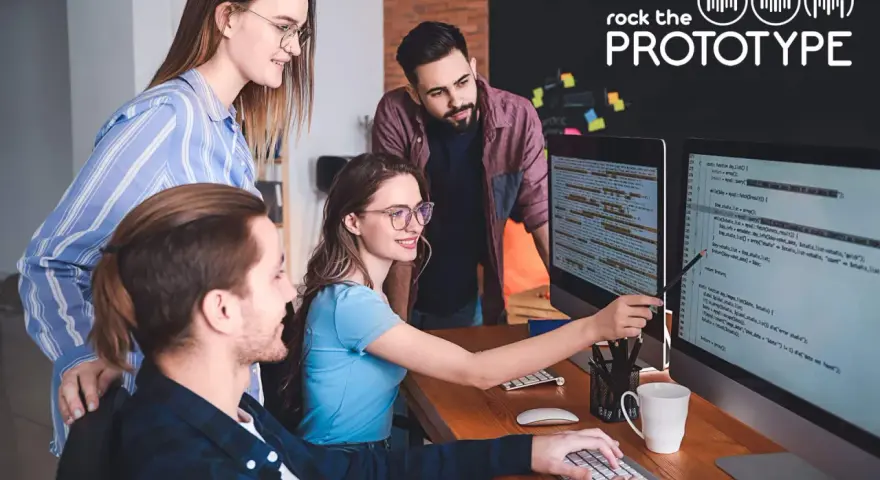 Ein Team von vier Personen arbeitet im **mob programming** an einem Projekt. Sie blicken auf zwei Bildschirme mit Code.