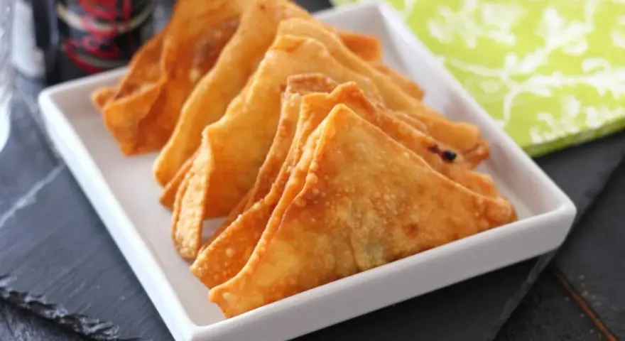 Wontons fritos dorados y crujientes en un plato blanco.