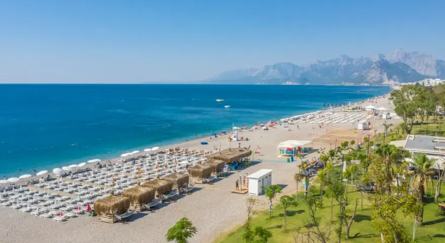 Piękna plaża z rzędami leżaków i parasoli, gdzie jest Antalya. Błękitne morze i góry w tle tworzą idealny krajobraz.