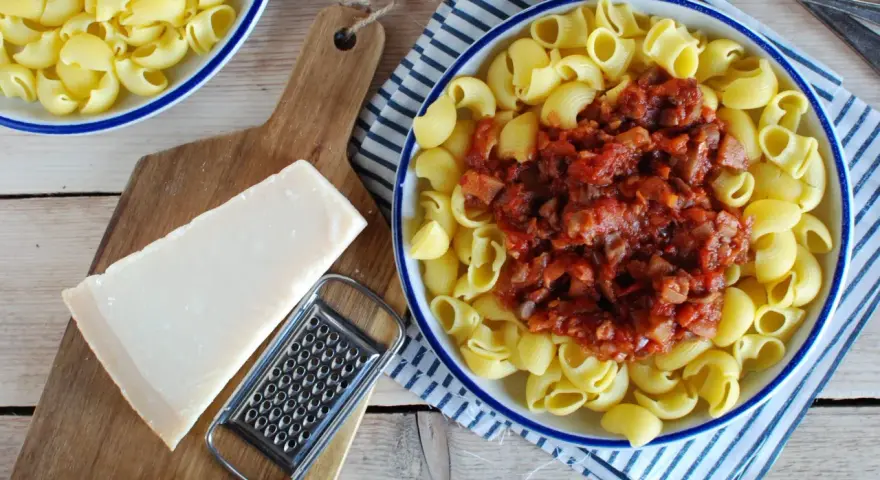 Makaron z sosem mięsnym, kawałek parmezanu i tarka na desce.