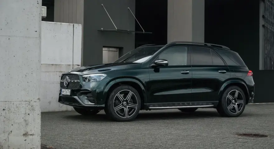 Elegancki, ciemnozielony Mercedes GLE 2025 zaparkowany przed nowoczesnym budynkiem.