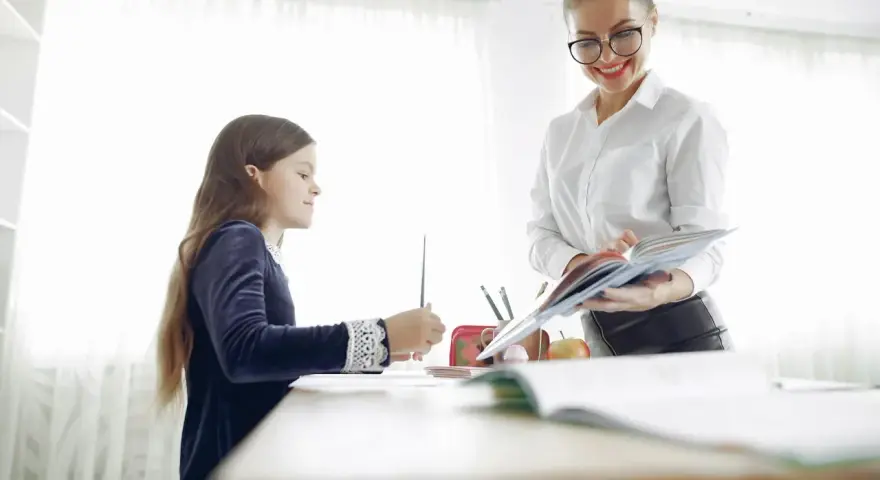 Nauczycielka pomaga dziecku z dysleksją w szkole, cierpliwie tłumacząc materiał z książki.