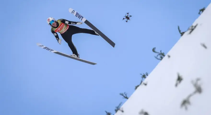 Skoczek narciarski w locie, z dronem w tle. Zastanawiasz się, ile waży skoczek narciarski, by osiągnąć taką odległość?