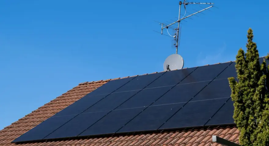 Dach mit Ziegeln, darauf schwarze Solarmodule für HEMS Photovoltaik. Eine Satellitenschüssel und Antenne sind ebenfalls zu sehen.