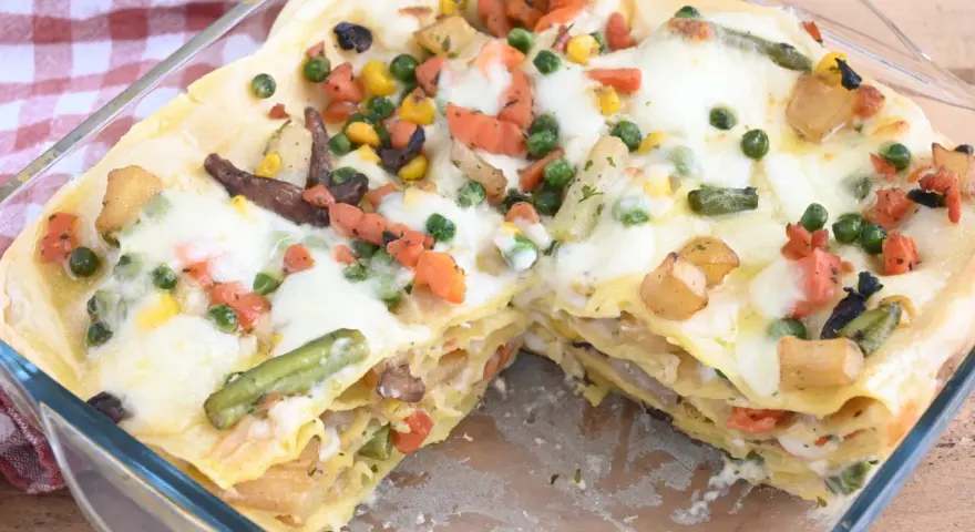 Lasagne di verdure dorate e filanti, con piselli, carote, patate e fagiolini, in una teglia di vetro.