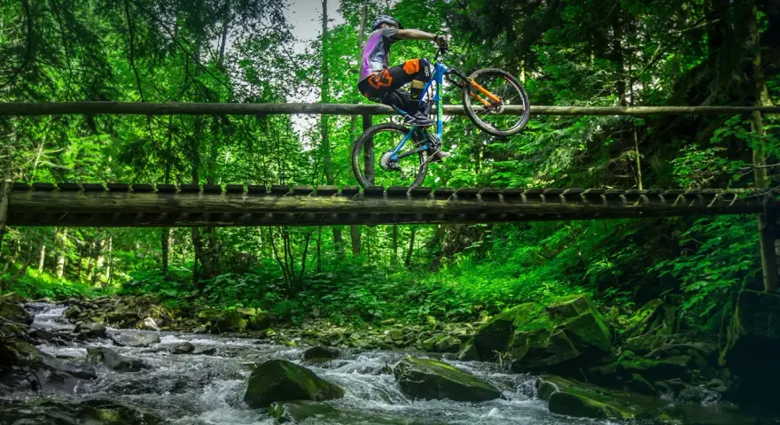 Rowerzysta na drewnianym moście nad potokiem, odkrywa nowe trasy rowerowe Zakopane.
