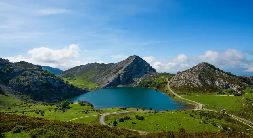 Lago azul rodeado de montañas verdes y caminos sinuosos, parte de la red de parques nacionales.