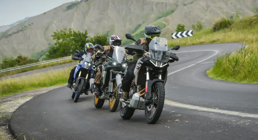 Quattro motociclisti in fila su una strada tortuosa tra colline verdi. Sei motociclista se ami l'avventura.