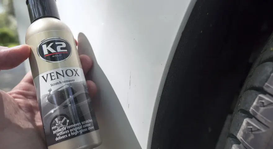 Jak usunąć głębokie rysy na lakierze? Butelka K2 VENOX Scratch remover obok białego lakieru z widocznymi zarysowaniami.