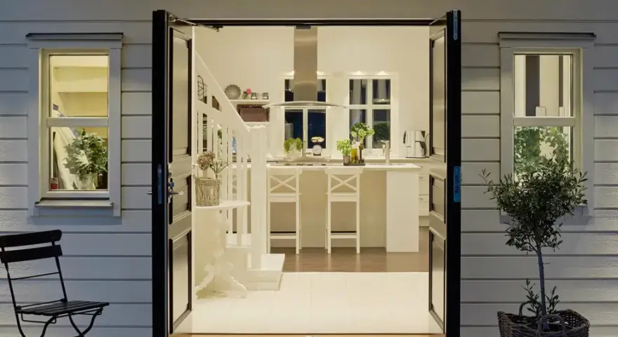 Välkomnande entré inspiration utomhus. Öppna dörrar leder in till ett ljust kök med köksö och trappa.