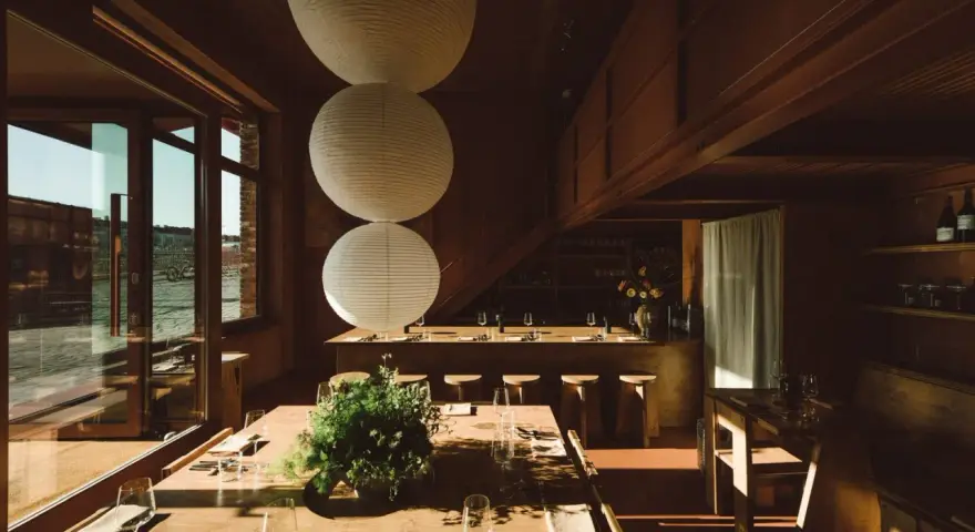 Gemütliches Restaurant in **Aerde Berlin** mit Holztischen, großen Papierlampen und Blick auf das Wasser.