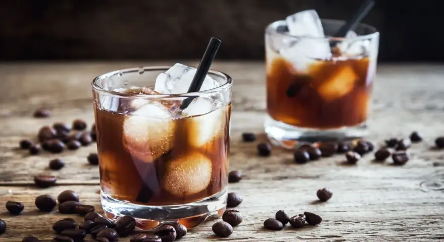 Dwa szklanki z lodem i ciemnym napojem, otoczone ziarnami kawy. Idealny czarny rusek drink na drewnianym blacie.