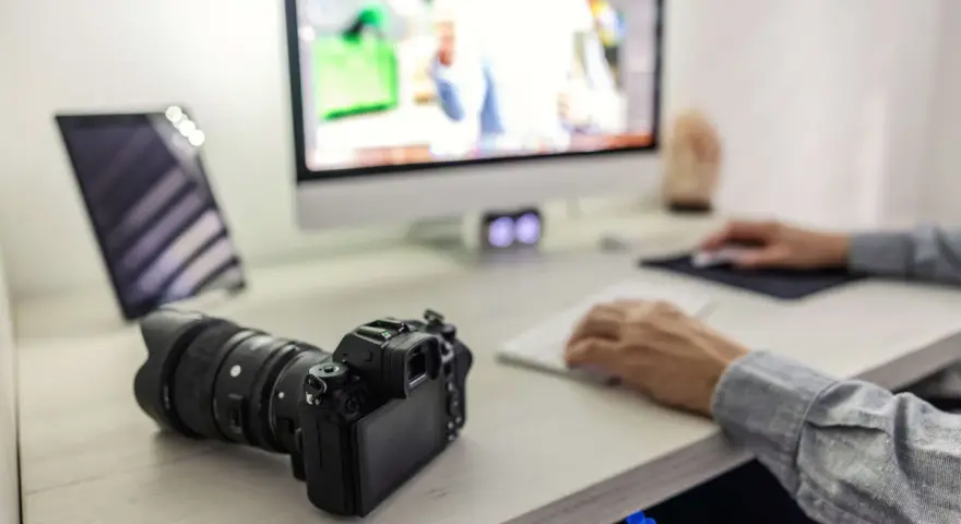 Aparat fotograficzny i tablet na biurku, obok komputera. Ułatwia to proces, jak przegrać zdjęcia z telefonu na komputer.