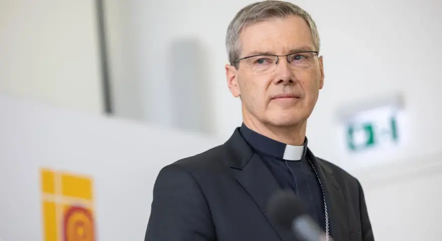 Ein Bischof mit Brille und Soutane spricht in ein Mikrofon. Die Frage "wer bezahlt den Bischof" wird hier nicht beantwortet, aber das Bild zeigt ihn bei einer öffentlichen Rede.