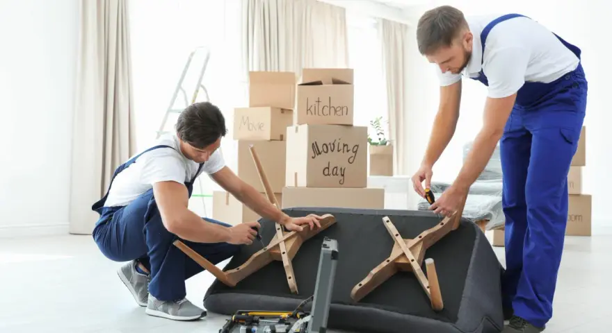 Deux déménageurs démontent un canapé fixe, outils à portée de main. Ils préparent le mobilier pour un déménagement.