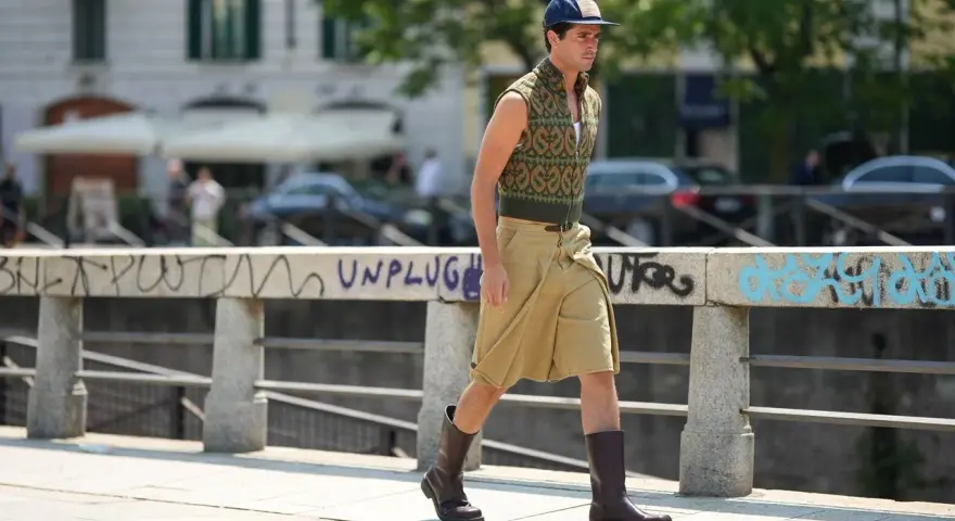 Uomo con un elegante outfit sportivo estivo: gilet a fantasia, bermuda color sabbia e stivali.