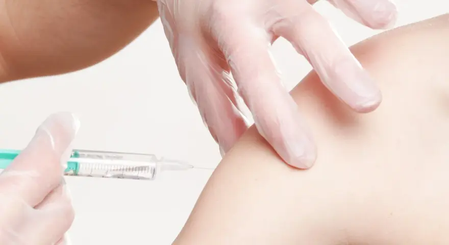 Ręka w rękawiczce wykonuje iniekcję domięśniową w ramię.