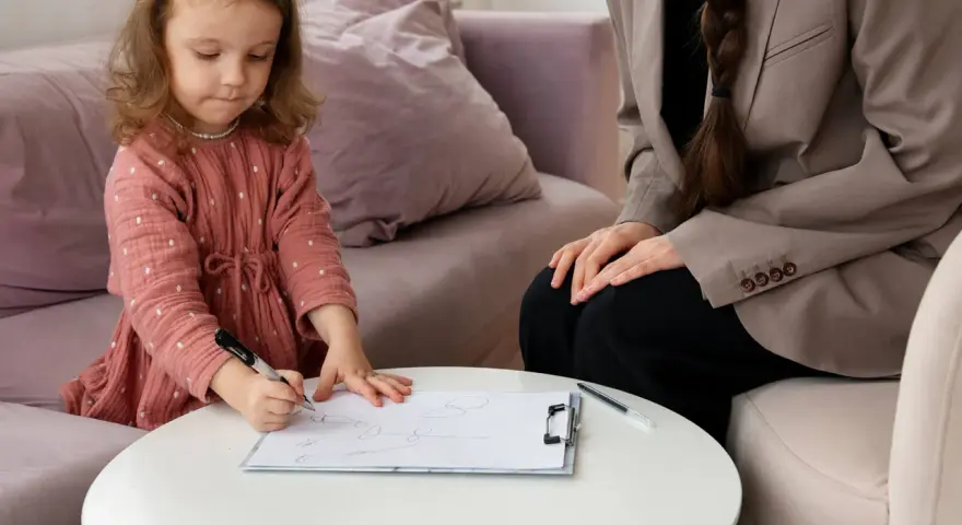 Mała dziewczynka rysuje, podczas gdy psycholog obserwuje. Proces ten może być częścią diagnozy ados.
