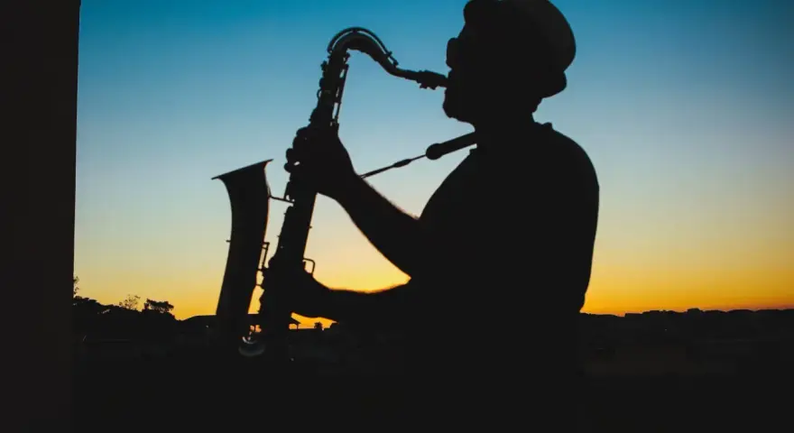 Sylwetka muzyka w kapeluszu grającego na saksofonie o zachodzie słońca. Prawdziwy mistrz, jeden z najlepszych bluesmanów świata.
