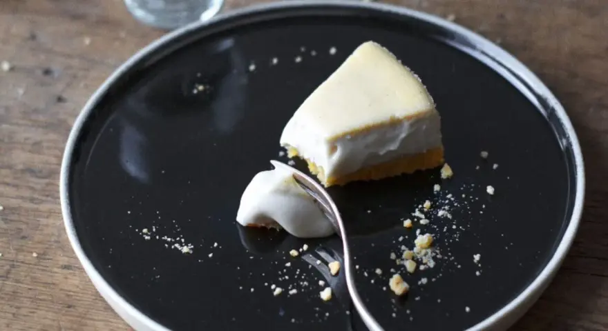 Un trozo de tarta de queso cremoso, con una porción ya probada, sobre un plato negro.