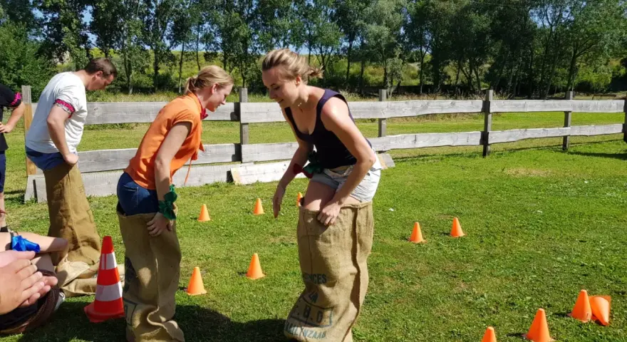 Des collègues s'amusent lors de jeux entre collègues de travail, sautant dans des sacs en toile de jute sur une pelouse verte.