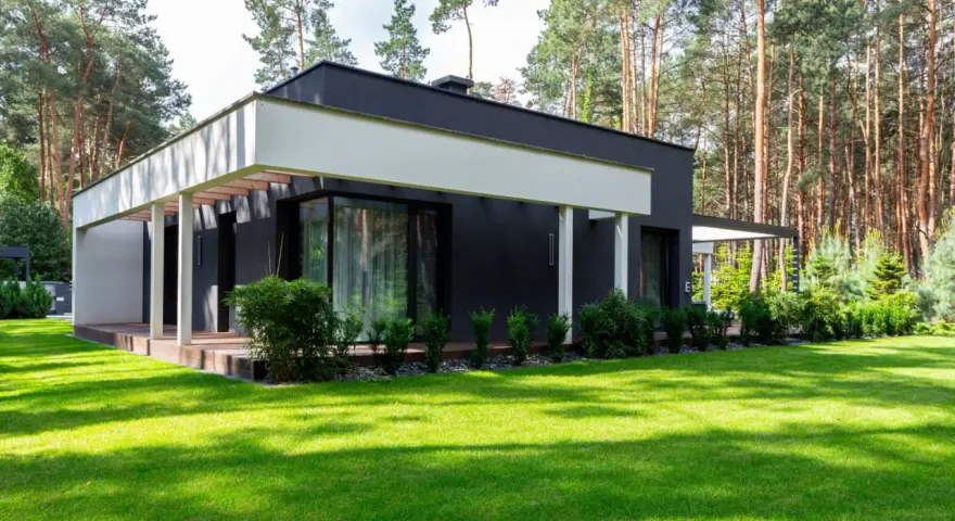 Nowoczesny dom z dużymi oknami i tarasem, otoczony zielonym ogrodem i lasem. Zastanawiasz się, jaki jest koszt budowy domu 150m2?
