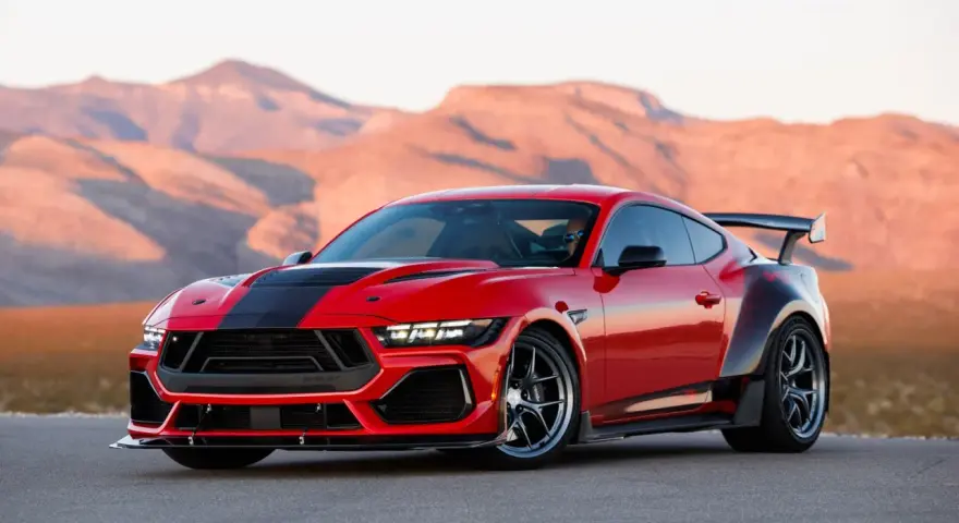Czerwony mustang shelby z czarnymi pasami i spojlerem na tle pustynnych gór.