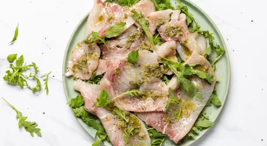 Deliziosi antipasti di pesce crudo, affettati sottili e conditi con erbe aromatiche e olio, serviti su un letto di rucola fresca.