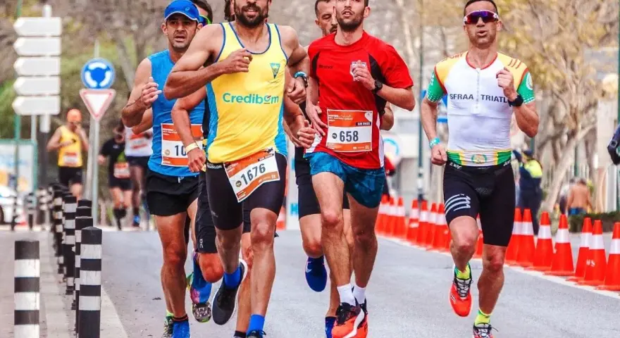 Atleti in gara, con pettorali visibili, corrono su strada. Le tabelle ripetute corsa principianti sono un ottimo modo per iniziare.