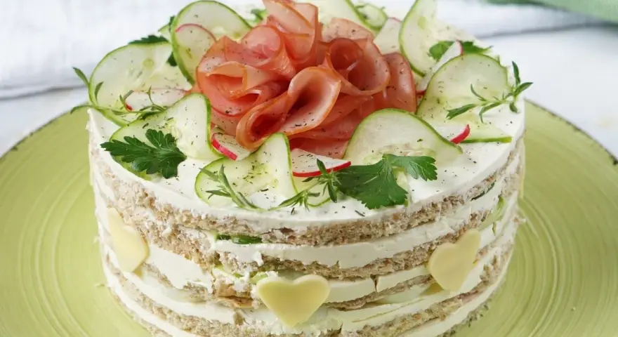 Herzhafter Kuchen mit Schichten aus Brot, Frischkäse, Gurken und Schinken. Dekoriert mit Radieschen, Kräutern und Käseherzen.