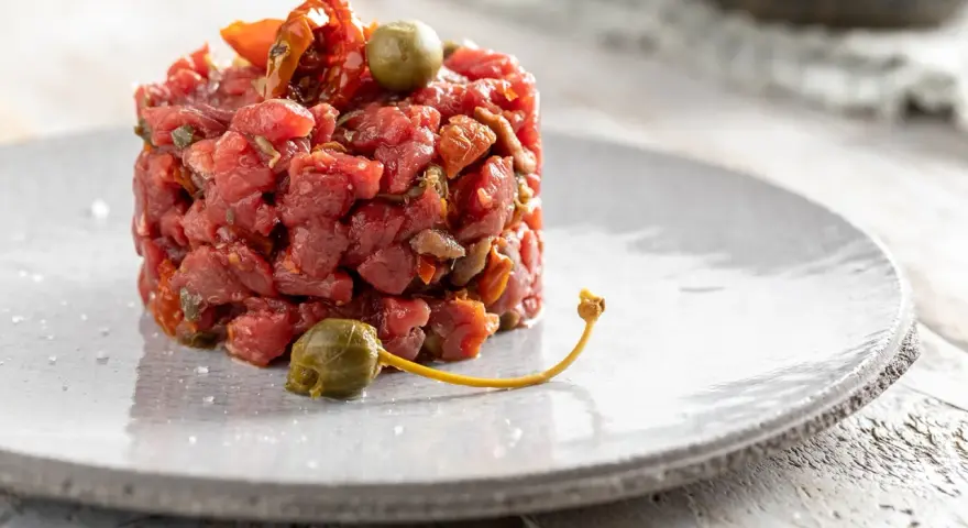 Deliziosa tartare di manzo, guarnita con capperi e pomodori secchi, servita su un piatto grigio.