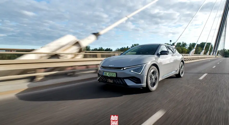 Szary Kia EV6 jedzie po moście w słoneczny dzień.