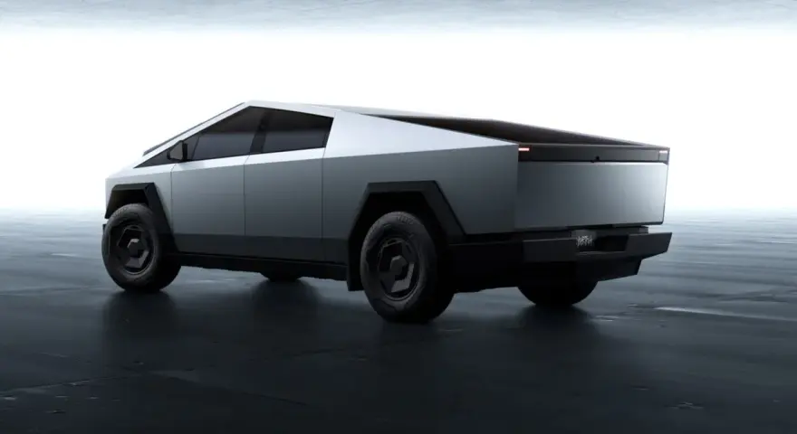 Futurystyczny Tesla Cybertruck w kolorze srebrnym, z ostrymi krawędziami i masywnymi kołami, prezentuje się na ciemnej, betonowej podłodze.