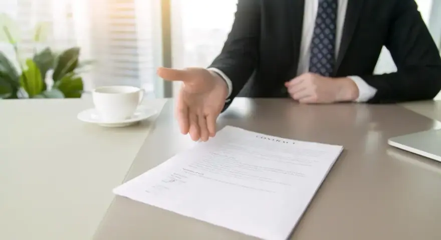 Biznesmen wyciąga rękę do uścisku nad dokumentem, symbolizującym rezygnację z pracy.