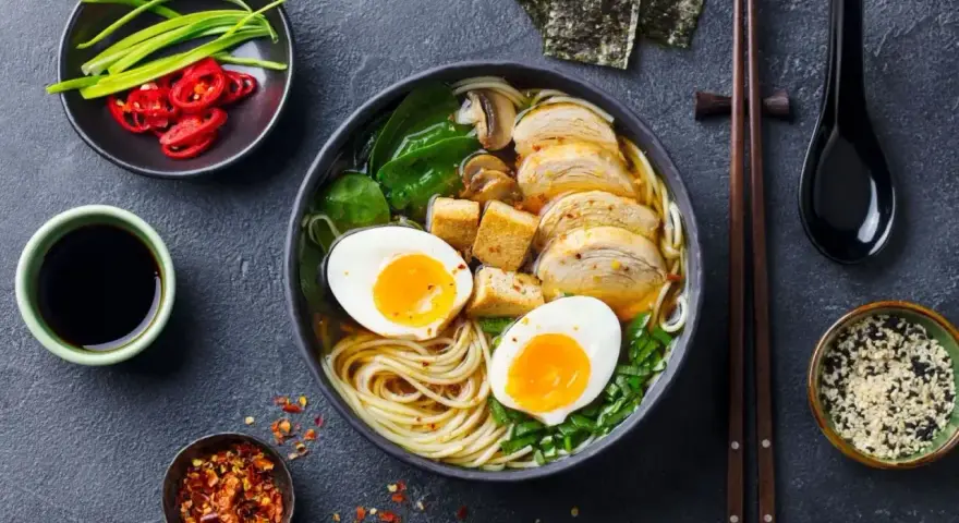 A miseczce aromatycznego ramenu z tofu, jajkiem na pół, kurczakiem i zieloną cebulką. Obok sos sojowy, chili i nori.