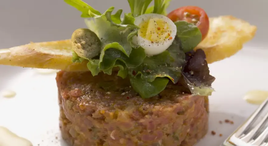 Un délicieux tartare de bœuf, garni d'une salade fraîche, d'un œuf de caille et de croûtons. Une recette parfaite pour un repas raffiné.