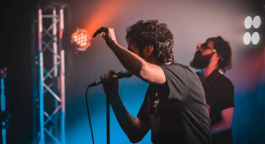 Ein Sänger mit Mikrofon auf einer Bühne, umgeben von Bühnenlichtern. Das ist, was Indie-Musik ausmacht: Leidenschaft und Energie.