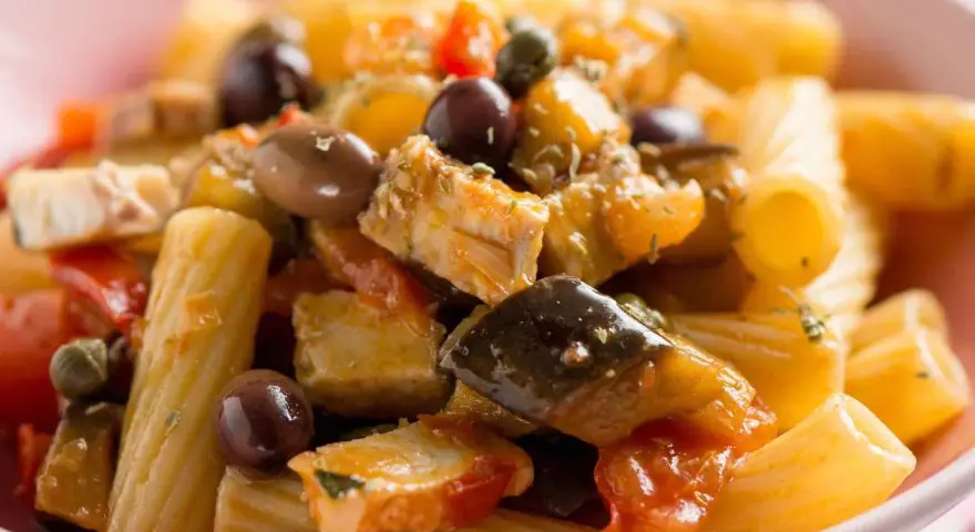 Un piatto invitante di pasta con pesce, arricchito da olive nere, capperi e verdure colorate.