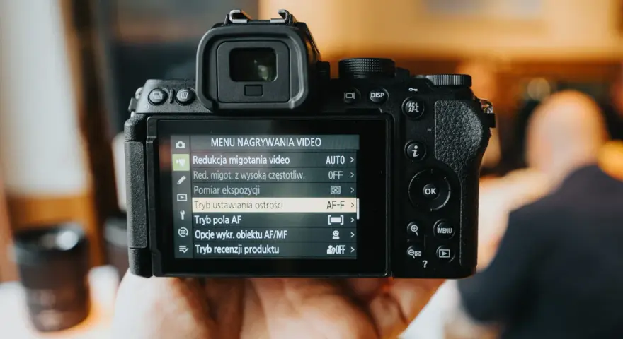 Dłoń trzyma aparat Nikon z włączonym menu nagrywania wideo, widoczne są opcje ustawień.