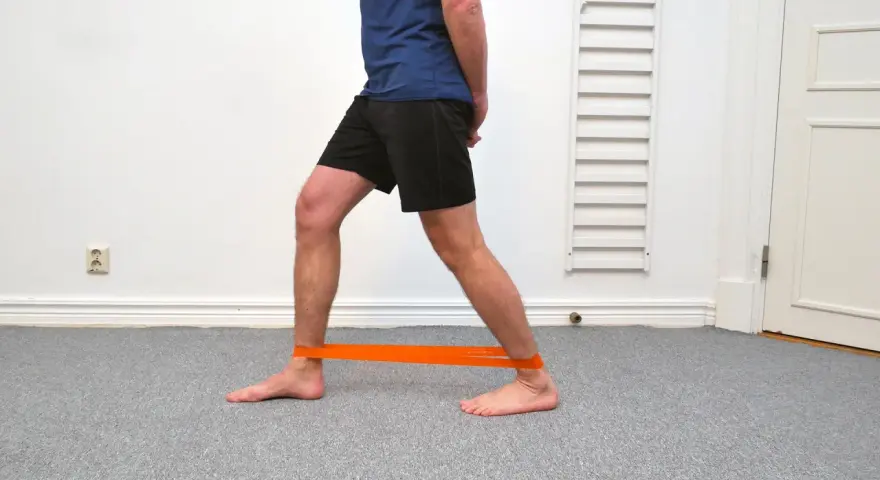 Man tränar för att stärka stela fotleder med ett orange träningsband runt anklarna.