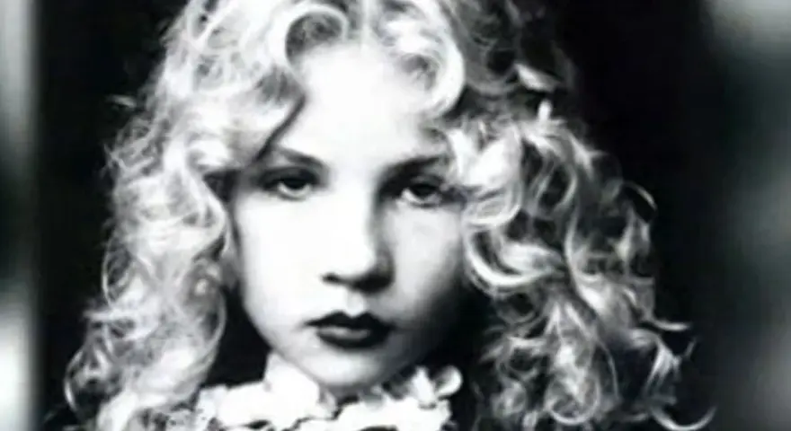 Portrait en noir et blanc d'Eva Ionesco enfant, aux boucles blondes et au regard intense.