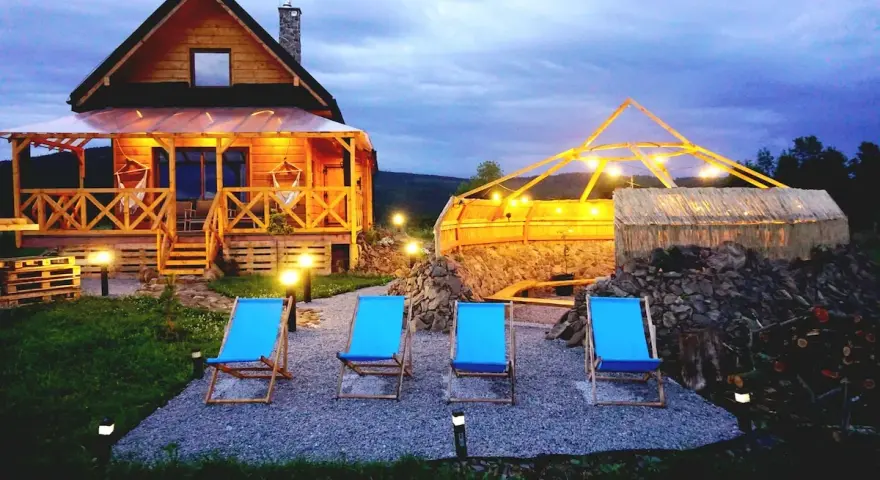 Drewniany domek z werandą, jacuzzi pod zadaszeniem i leżakami w malowniczej okolicy.