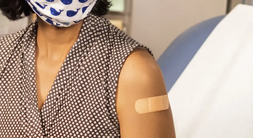 Osoba w maseczce z wielorybami ma plaster na ramieniu po szczepieniu. Dbanie o zdrowie, w tym szczepionka HPV, to ważny krok.