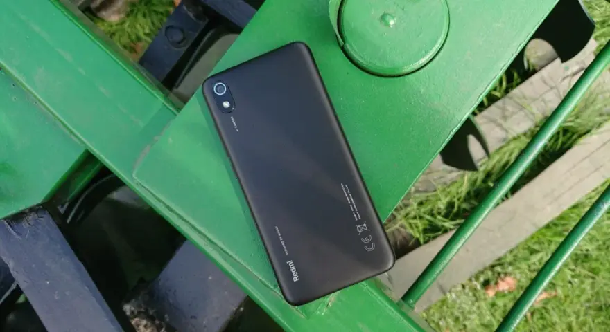 Czarny telefon Xiaomi Redmi 7 leży na zielonej, metalowej ławce.