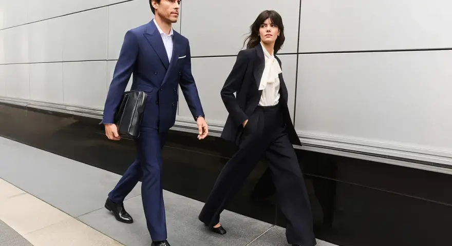 Para idąca w eleganckim business attire, mężczyzna w granatowym garniturze, kobieta w czarnym.