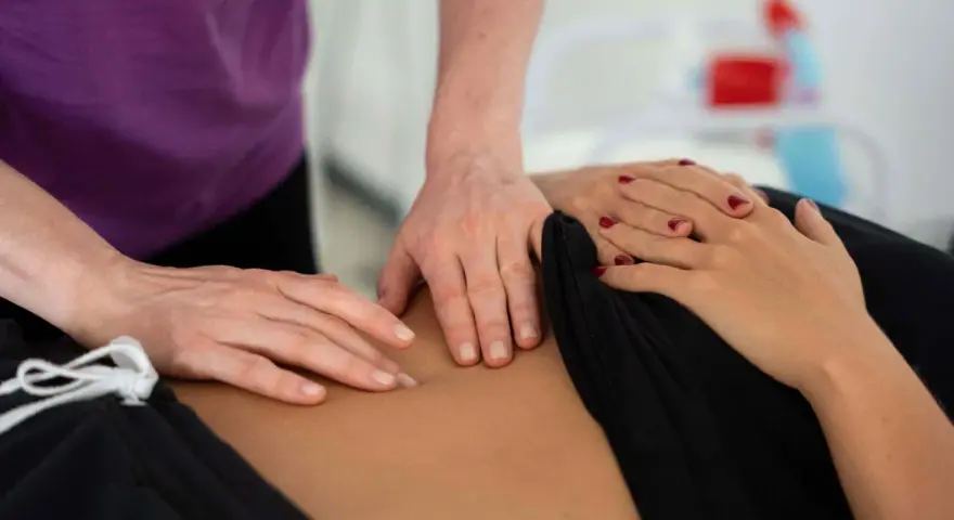 Dłonie terapeuty wykonujące masaż brzucha pacjentki.