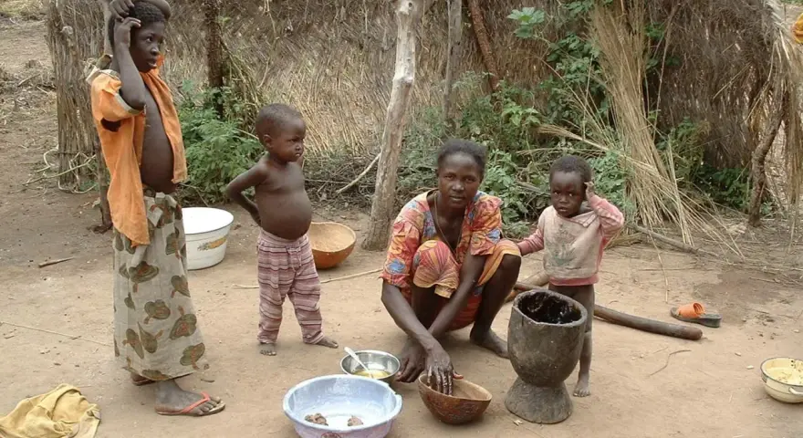 Dzieci i matka w tradycyjnej chacie w Burkina Faso. Kobieta przygotowuje posiłek, a dzieci obserwują.