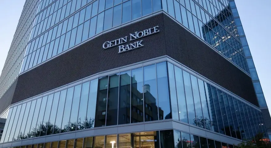 Nowoczesny budynek banku z napisem "GETIN NOBLE BANK". W szklanej fasadzie odbijają się inne budynki i drzewa.