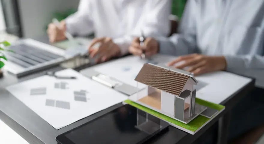 Model domu na biurku, gdzie trwa dyskusja o gospodarce przestrzennej.